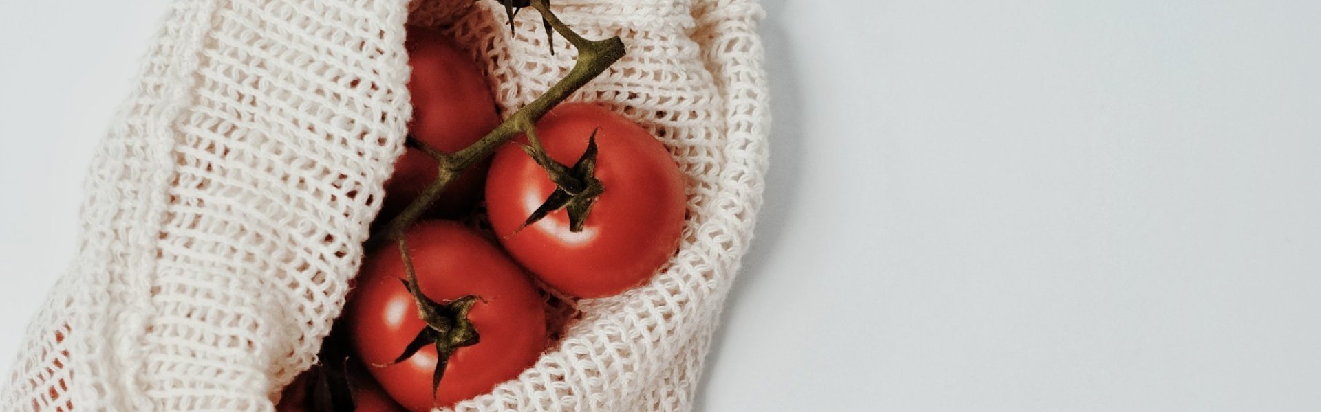 Trostomaten op het keukenaanrecht samen met een houten lepel en groentennetje met extra tomaten.